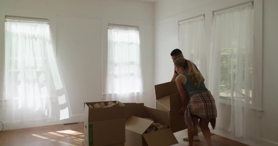 Tired couple moving boxes into an empty living room