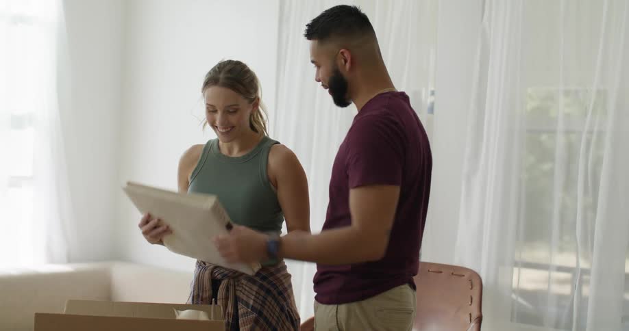 Two people are unpacking a photo album in a welllit room with white curtains and a beige couch