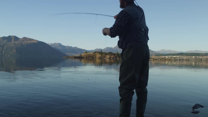 Man with the hat fly fishing while standing in shallow water