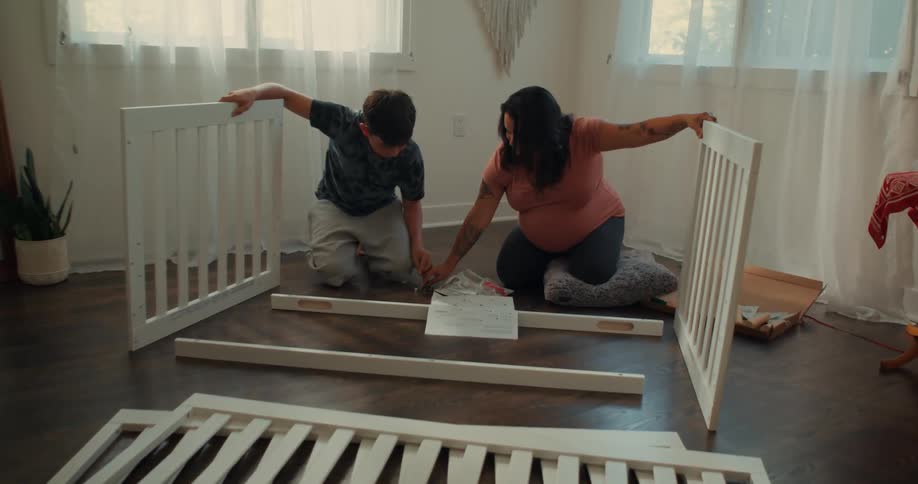 Pregnant mother and teenage son assembling a crib together in babies nursery