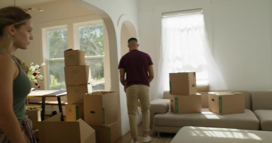 Couple organizing furniture in a room of their house with several moving boxes