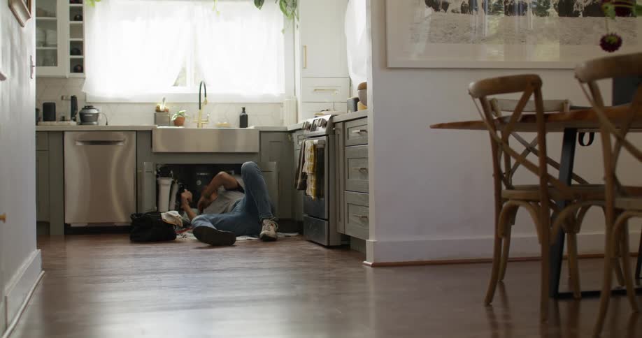 Man lying in the kitchen tidying the sink