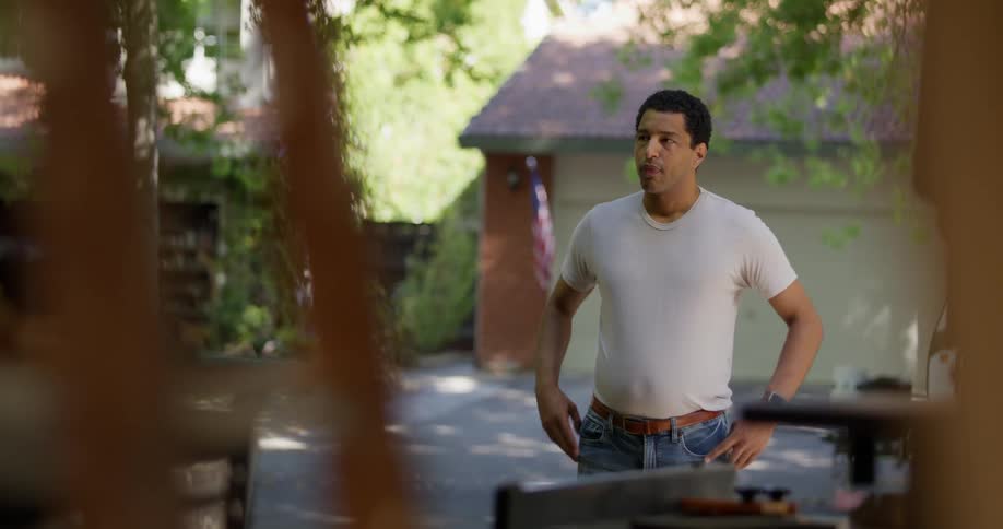 A man stands in front of a garage with his arms on his hips