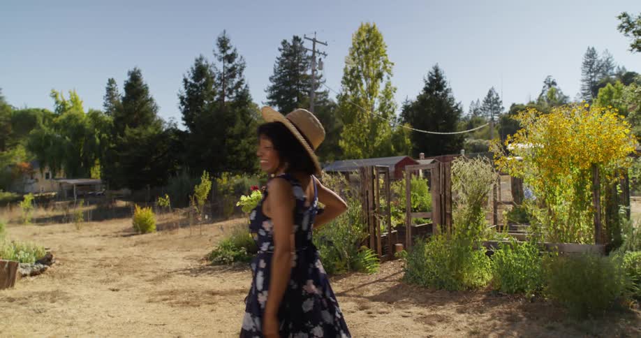 A woman in a floral dress passes by a man cleaning a trailer on her way to the garden