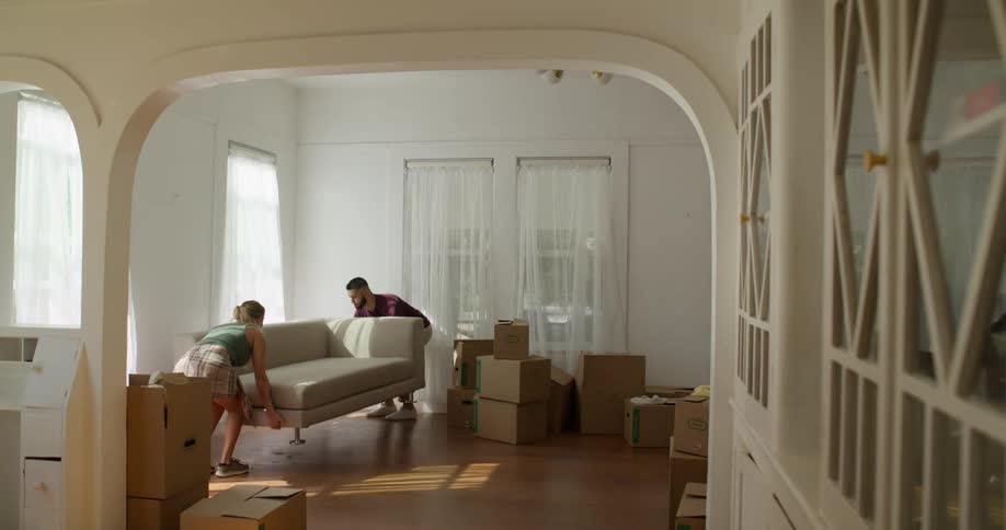 Couple in a living room with moving boxes arranging a sofa in a corner