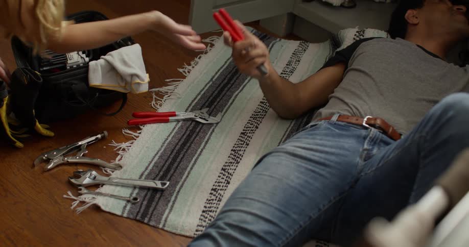 Woman handing tools from a bag to a man lying on the floor