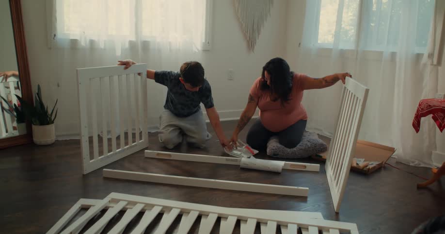 A pregnant mom and her son assemble a crib in a room