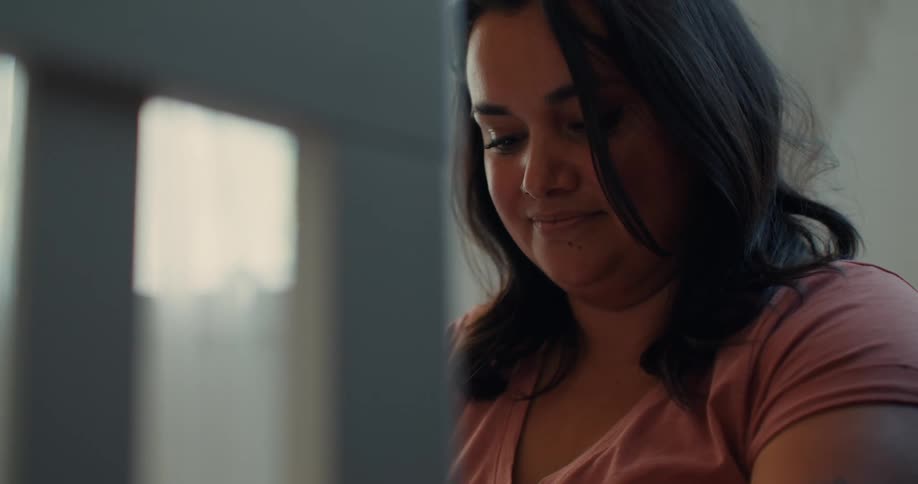 Pregnant woman with wavy hair pink t shirt and tattoos gazes at the new crib