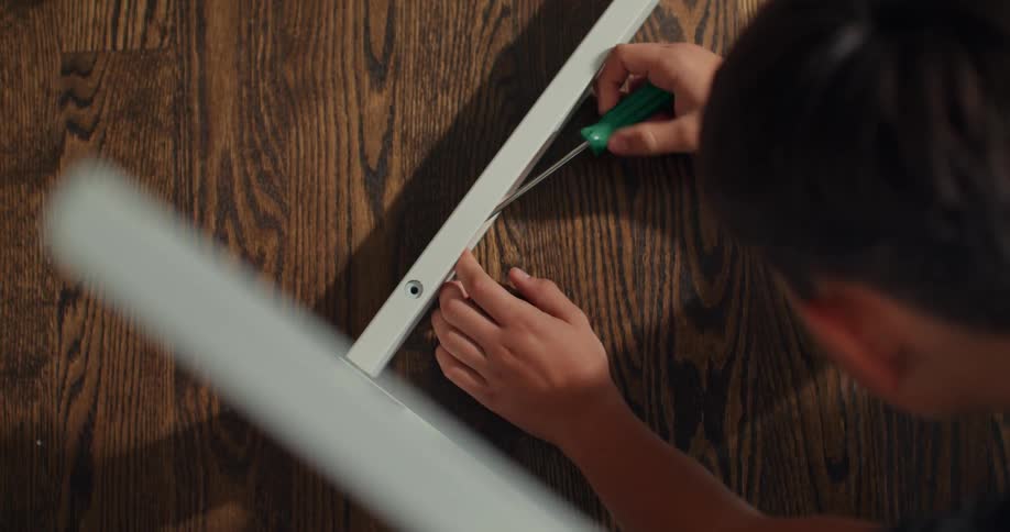 A boy is using a screw driver on the crib frame