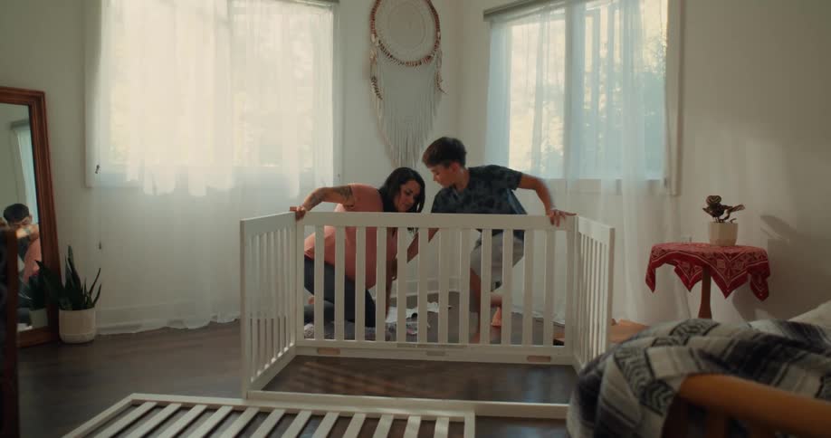 Mother and son are assembling a white crib in a welllit room with large windows