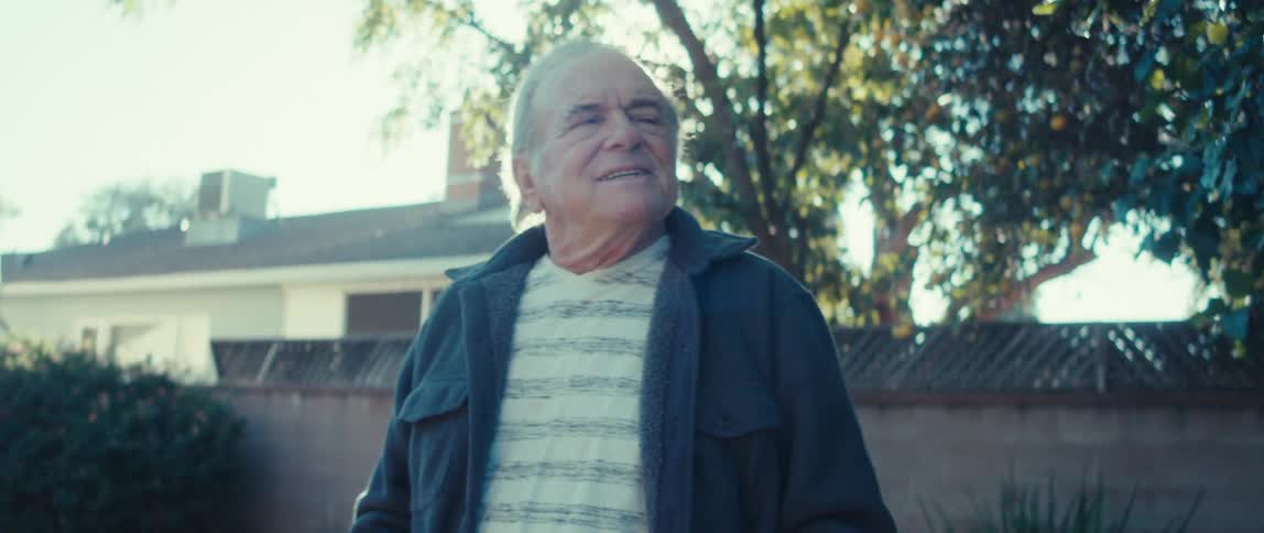 An elderly man stands in the backyard on a sunny day