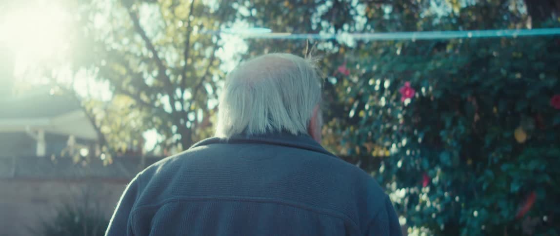 Elderly man walking through a yard with trees