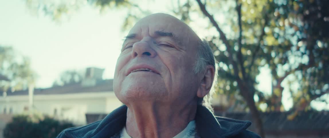 An elderly man stands outdoors closes his eyes and meditates