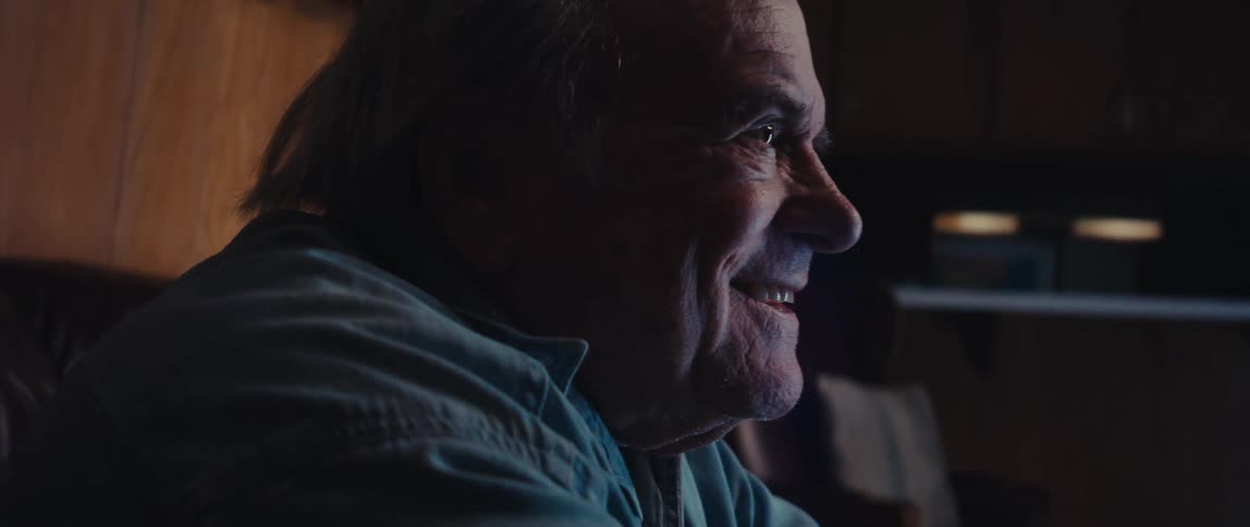 A man leans forward smiling while watching television