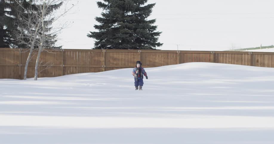 A young child walks across a snowy yard