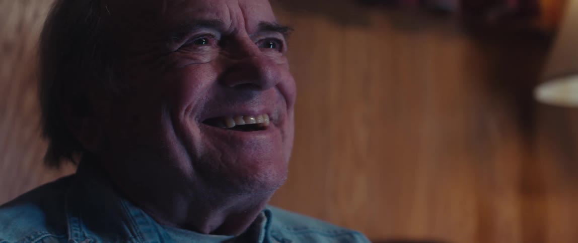 A closeup of an elderly man laughing while watching television at home