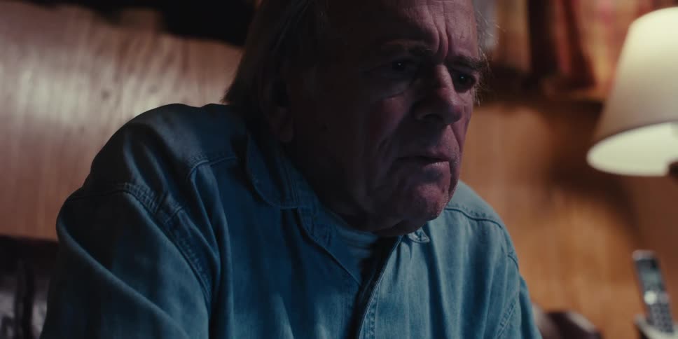 Elderly man sitting next to a window takes off his eyeglasses while thinking