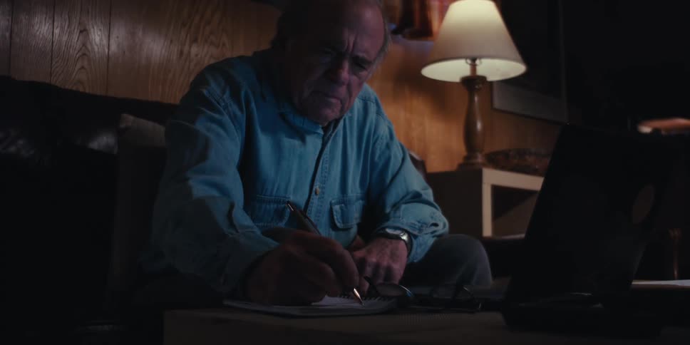 A man types on his laptop then writes a note