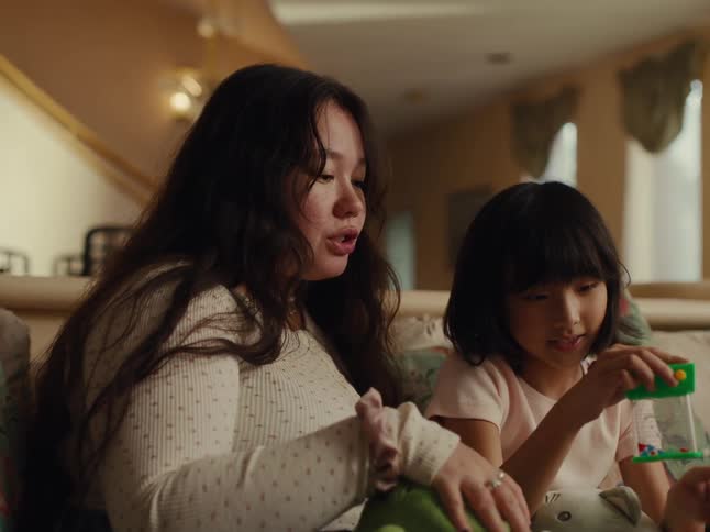 Mother guides daughter in playing with a toy while they sit at home