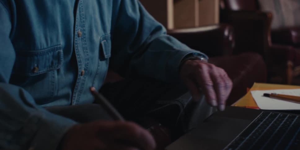 Person sitting in front of an open laptop and writing with a pen on a notepad next to it