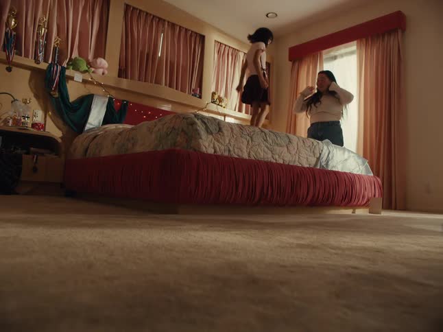 A young girl jumps on a bed and then begins playfully fighting with an adult who was previously lying in it