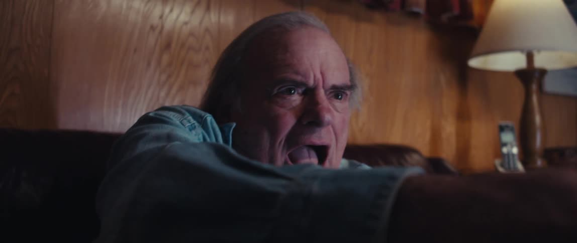 The face of an elderly gentleman who is sitting on a sofa and is very excited while smiling looking forward