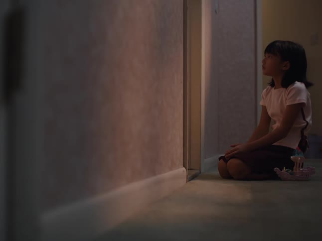 A little girl sitting on the floor inside a house with a sad look and then she turns around and starts playing with a toy that is on the floor