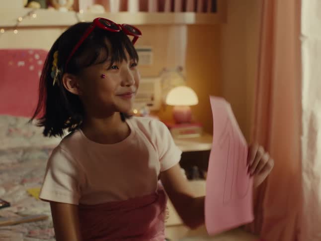 A happy girl sits on her bed proudly showing a paper with a large number ten written on it