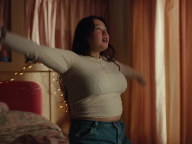 Mother adjusts her shirt before lying down on a bed and her daughter makes a flip onto the same bed