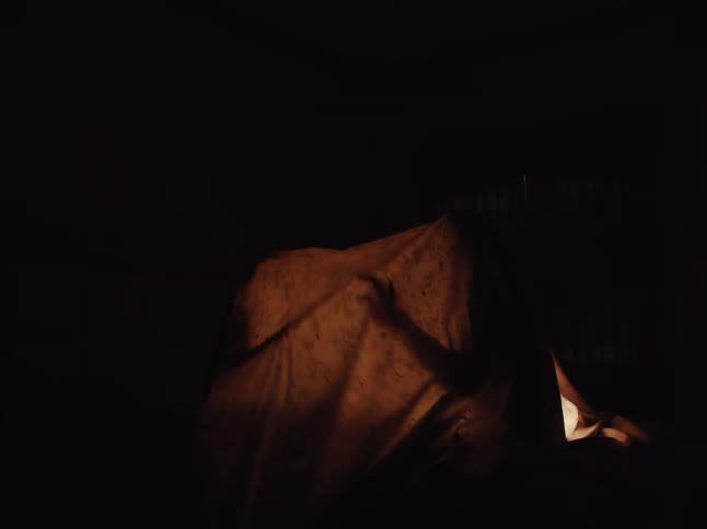 Shadow of two people under a sheet in a dark room playing
