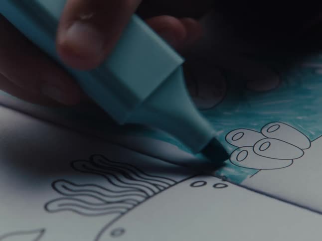 A closeup view of a hand using a blue marker to color a page in a coloring book