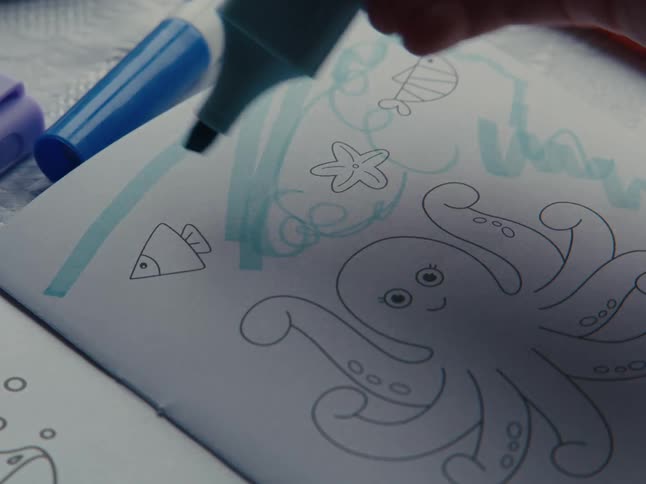 A blue pen being drawn on a white sheet of paper with a drawing of an octopus