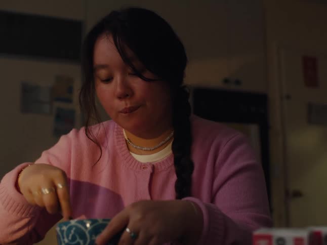A young woman in pink clothes is stirring a utensil inside a blue bowl