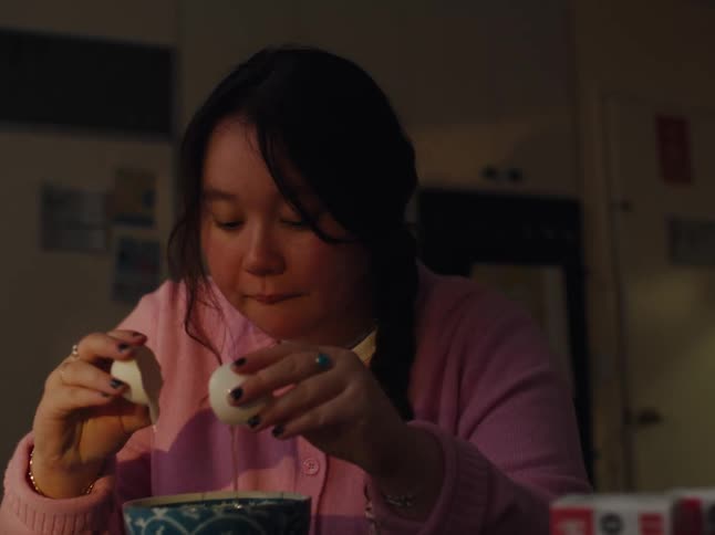 A teenage girl in a pink shirt is cracking an egg into a bowl on a table