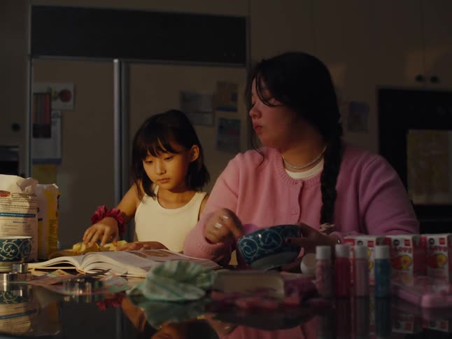Woman cooking in a bowl while sitting down and a girl coming to her side