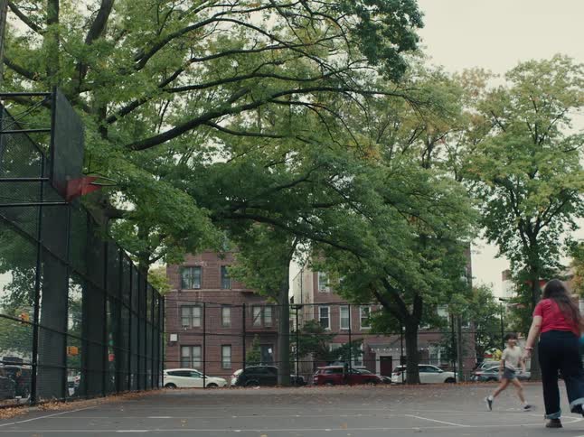 A teenage girl in a red shirt is shooting a blue basketball into a hoop