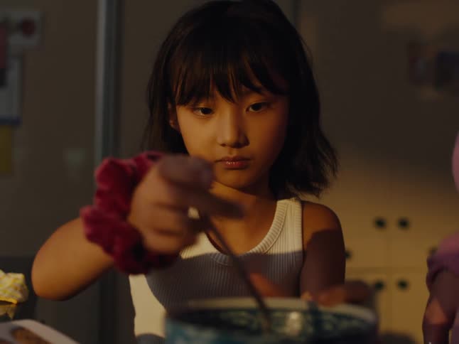 A girl wearing a white tank top and a red scrunchie on the wrist is stirring something in a bowl
