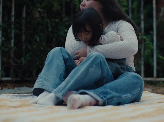 Two young people likely siblings are seated and hugging closely on a blanket