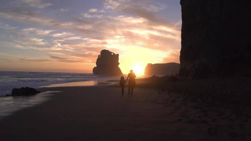 A person and child walk down a beach at dusk