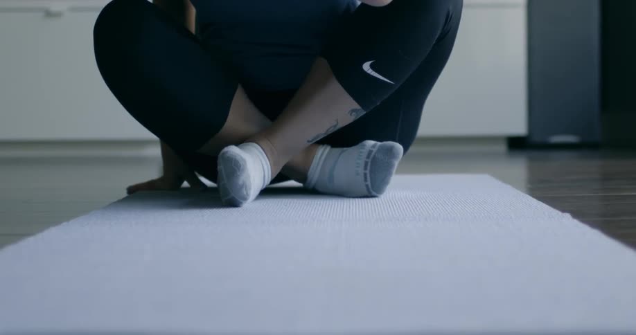 A woman sits down crossed-legged on a mat in a room