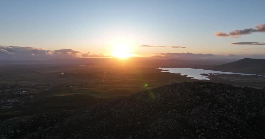 The sun sets over a landscape with rolling hills and a lake