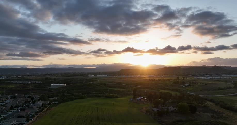A golden sunset illuminates a rolling landscape dotted with farms and distant mountains