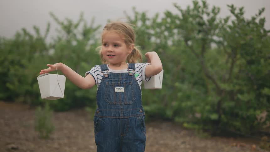 Little girl holding two small boxes while standing in a natural environment