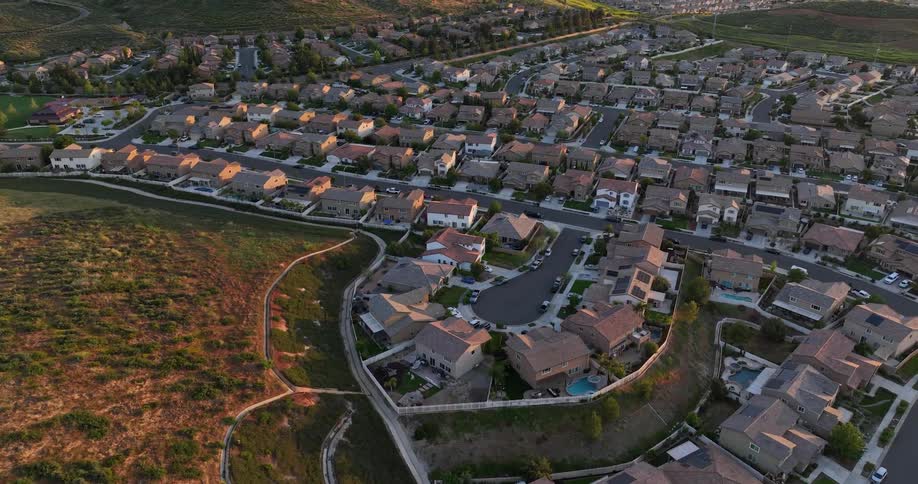 A sprawling suburban neighborhood nestled in a valley with rolling hills and a distant city skyline in the background