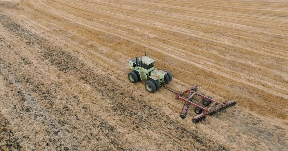 An aerial view of a green tractor with a combine harvester attached to the back that is cutting grass from the ground