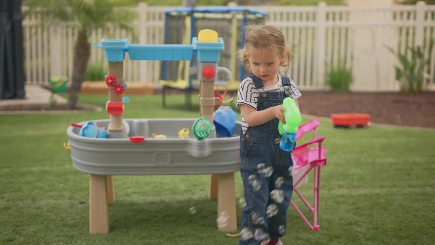 A young girl plays with a bubble gun in her backyard