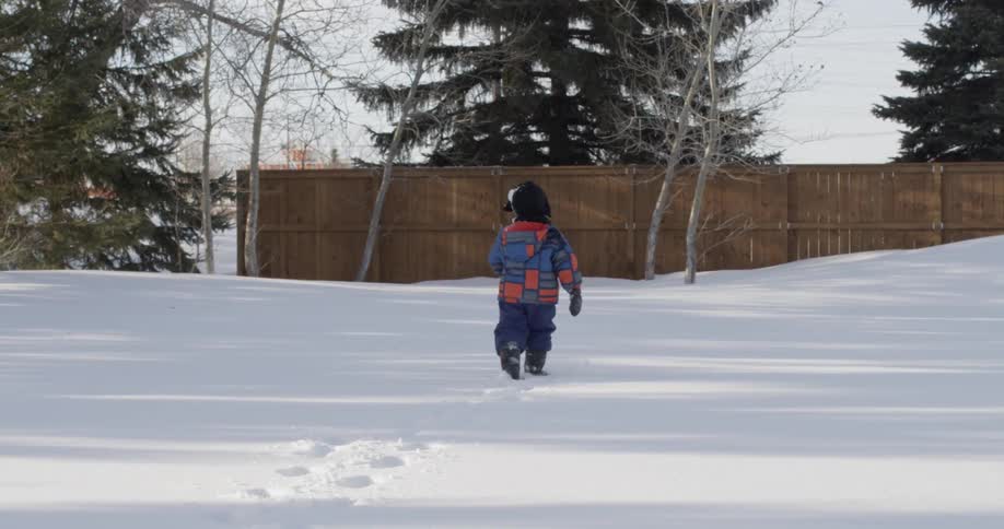 A young boy walks across a snowy yard