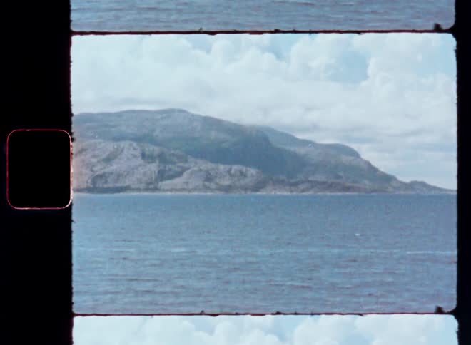 A rocky coastline with a mountainous landscape in the distance under a cloudy sky