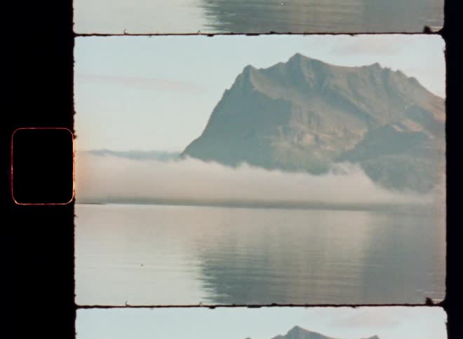 A serene mountain landscape with a prominent peak reflected in a calm lake partially shrouded by a layer of mist