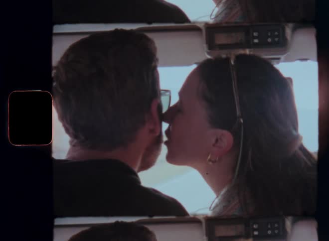 A woman kisses a man driving a car on a road trip captured on vintage film